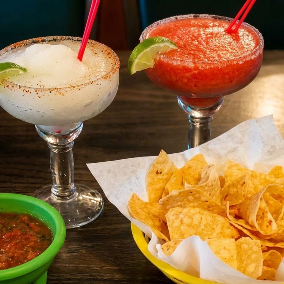 Two frozen margaritas, one white and one red, with a basket of tortilla chips and salsa.