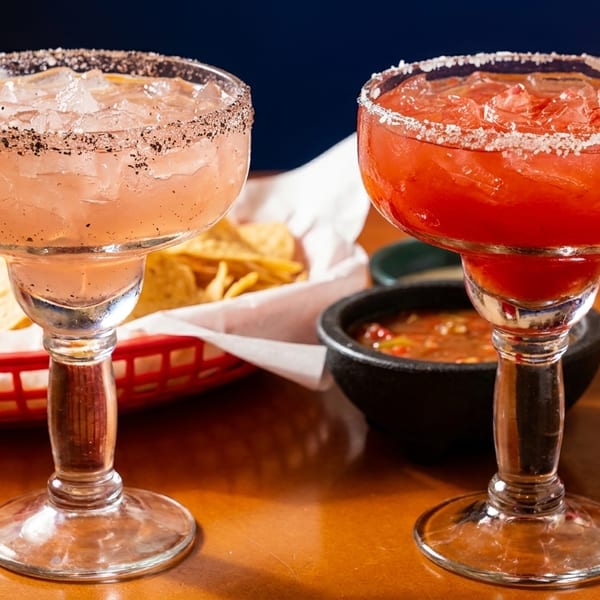 Two margaritas, one pink and one red, with lime slices and salted rims, next to chips and salsa.